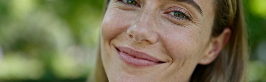 Portrait d'une femme caucasienne avec une peau saine et un sourire confiant, éclairée par une lumière naturelle douce
